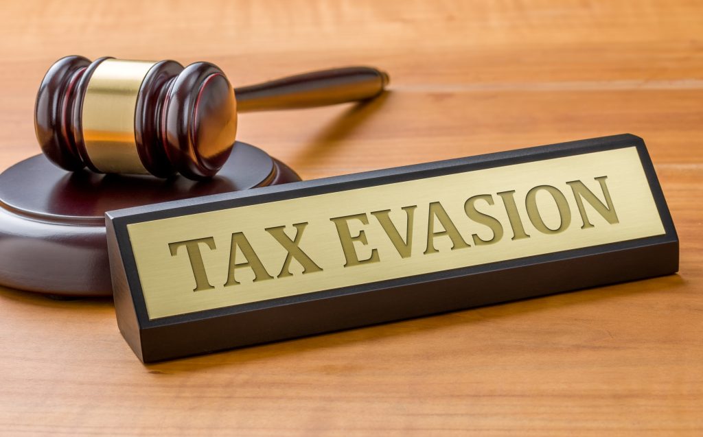 Palunya hakim dan papan bertuliskan 'Tax Evasion' di atas meja kayu, simbol pelanggaran hukum perpajakan